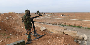 Ein Soldat, der ein Gewehr in der Hand hält, blickt in eine braun-graue Ebene