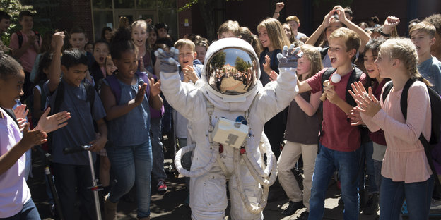 Viele Kinder stehen um einen Jungen im Astronautenanzug und klatschen