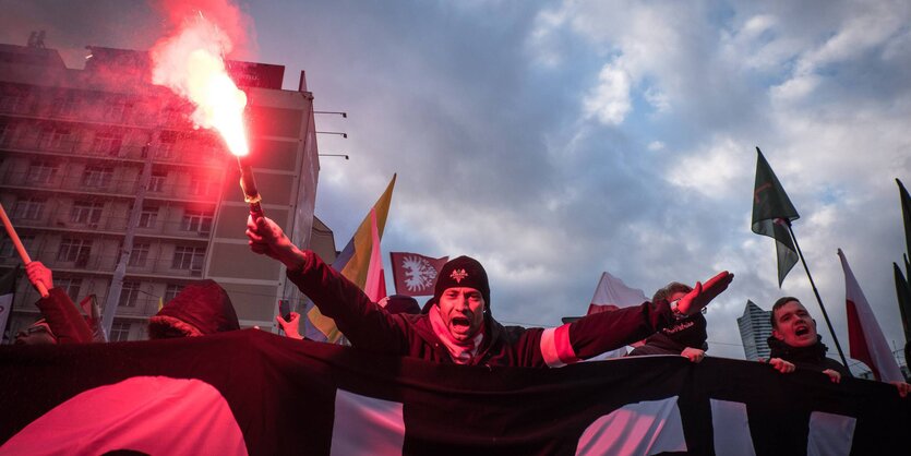 Ein Mann hinter einem Banner hält einen Bengalo in die Luft.