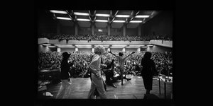 Schwarz-Weiß-Foto von einer Bühne in ein voll besetztes Auditorium
