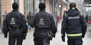 Ein Mitarbeiter des Ordnungsamtes und zwei Polizisten laufen durch eine Innenstadt