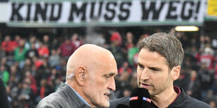 Hannover-96-Präsident Martin Kind gibt in der HDI-Arena ein Interview, im HIntergrund ist ein Banner mit dem Text "Kind muss weg" zu sehen.