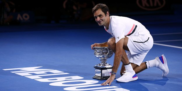 Roger Federer kniet auf dem Hallenboden neben einem Pokal nieder