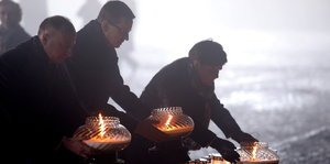 Zwei Männer und eine Frau stellen Kerzen an einer Gedenkstätte ab