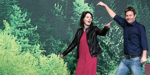 Eine Frau und ein Mann, der Mann zeigt auf die Frau, der Hintergrund sieht aus wie grüner Wald