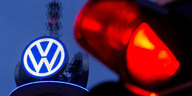 ein rotes Ampellicht leuchtet vor einem VW-Symbol vor dunkelblauem Abendhimmel