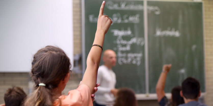 Kinder sitzen vor einer Tafel und heben die Hand