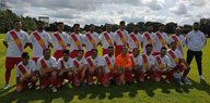 22 Spieler und ein Trainer der Mannschaft des FC Exidxan. Die Spieler tragen rot-weiße Trikots mit einer Sonne vorne drauf.