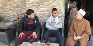 ein muslimischer Gelehrter sitzt neben zwei Jungs in einem Café