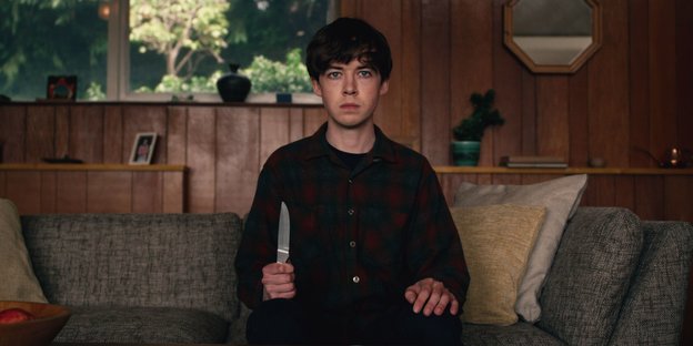 Ein junge sitzt mit einem Messer in der Hand auf einem Sofa.