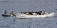 Eine Gruppe von Flüchtlingen sitzt in einem weißen Boot, dem sich ein Rettungsboot nähert