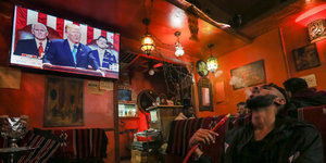 Ein Mann raucht in einem Café eine Shisha, im Hintergrund läuft Trumps Rede auf einem Fernseher