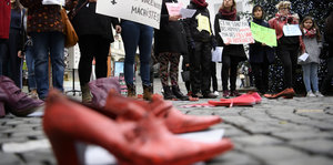 Frauen und Mädchen halten Schilder hoch, im Vordergrund ein rotes Paar Schuhe