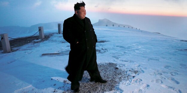 Kim Jong Un steht breitbeinig im Eis und lächelt