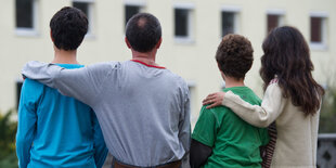 Eltern und Kinder sind von hinten fotografiert, die Eltern legen ihren Arm um die Kinder