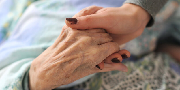 Eine junge Frau hält die Hände einer alten Frau
