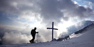 Silhouette einer Skiläuferin vor einem Kreuz im Schnee