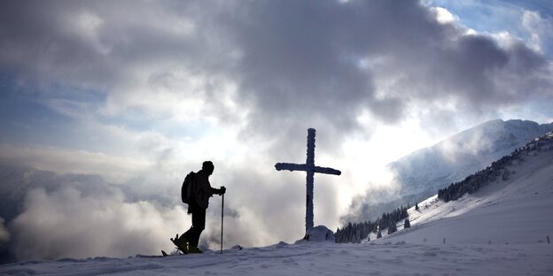 Silhouette einer Skiläuferin vor einem Kreuz im Schnee