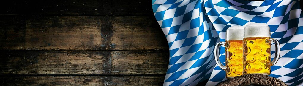 Holzvertäfelung mit Fass, darauf zwei Maß Bier und im Hintergrund die blau-weiße Bayernflagge