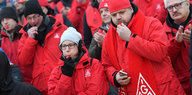 Männer und Frauen in roten Jacken blasen in Trillerpfeifen