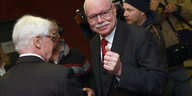 Zwei alte Männer mit schwarzen Brillen und Anzügen werden umringt von Journalisten mit Kameras und Mikrophonen.