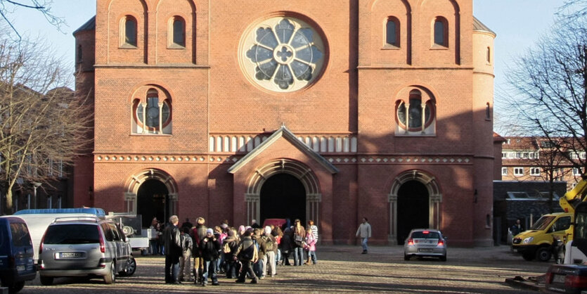 Menschen stehen auf einem Platz vor einer Kirche aus roten Backsteinen.