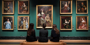Drei Frauen sitzen vor mehreren Gemälden in einem Museum