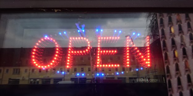 Hinter einer Fensterscheibe leuchtet in rot das Wort "Open".