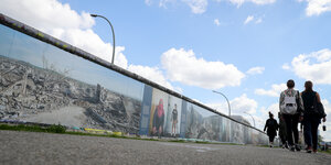 Leute laufen neben einem Stück Berliner Mauer lang