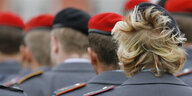 Mehrere Soldaten stehen in mehreren Reihen und tragen rote Mützen, eine Soldatin hat verwuschelte Haare