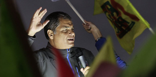 Rafael Correa hält eine Rede, viele Menschen um ihn schwenken Fahnen