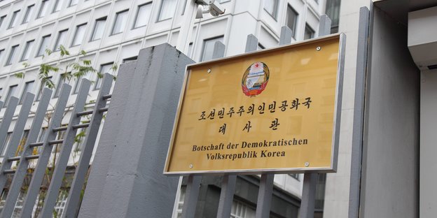 Das Foto zeigt ein Schild an einem zaun. Auf dem Schildt steht "Botschaft der Demokratischen Volksrepublik Korea" unter einer Reihe von koreanischen Schriftzeichen