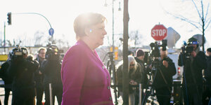 Angela Merkel schreitet im magentafarbenen Sakko als Schatten vor gleißender Sonne nach rechts