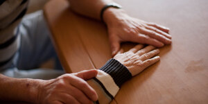 Hände führen die Hand einer älteren Person über eine Tischplatte