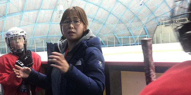 eine Frau steht umringt von Eishockeyspielerinnen in einer Eishalle