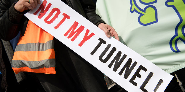 Jemand mit Leuchtweste hält ein Schild in der Hand "Not my Tunnel"
