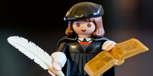 Eine Spielzeug-Figur mit Federkiel, Buch, schwarzem Umhang und schwarzer Mütze.