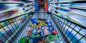 Ein Einkaufswagen mit vielen Lebensmitteln fährt durch einen Supermarkt