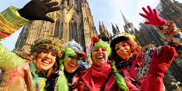 Vier verkleidete Frauen winken vor dem Kölner Dom