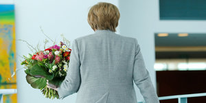 Angela Merkel entfernt sich von der Kamera mit einem Blumenstrauß in der Hand