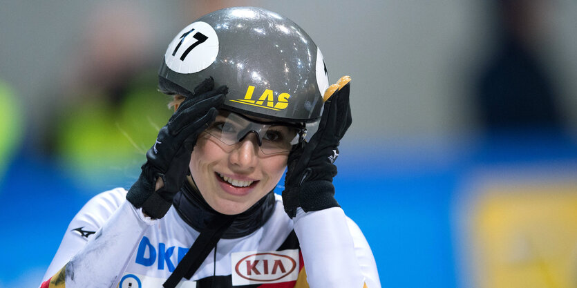 Eine Frau (Gesicht und Oberkörper) mit Sportbrille und Helm. Mit ihren Händen hält sie den Helm.