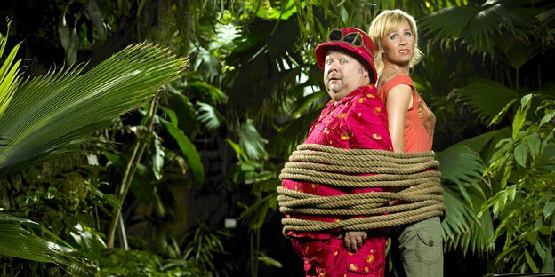 ein Mann und eine Frau sind Rücken an Rücken im Dschungel gefesselt