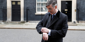 Brexit-Hardliner Jacob Rees-Mogg wartet vor der Residenz der Premierministerin und schaut auf die Uhr.