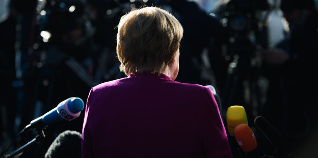 Angela Merkel steht im Dunkeln vor Mikrofonen