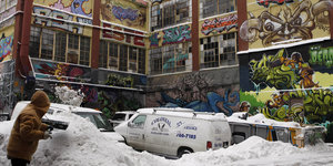 Ein eingeschneites Auto steht vor einem bemalten Gebäude