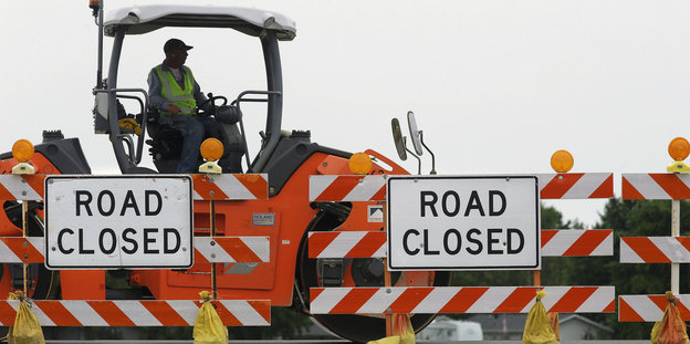 Ein Mann auf einer Baustelle, davor Schilder mit der Aufschrift "Road Closed"