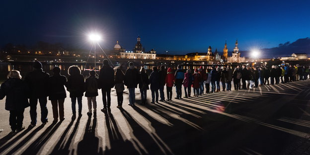 eine Menschenkette am Flussufer, im Hintergrund die historische Innenstadt Dresdens