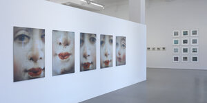 Eine Wand mit fünf Portraitfotos von einer Frau mit rot geschminkten Lippen.