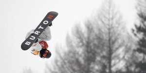 ein Mensch auf einem Snowboard fliegt kopfüber an Bäumen vorbei