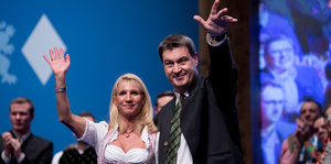 Markus Söder und seine Frau Karin Baumüller-Söder winken von einer Bühne herab